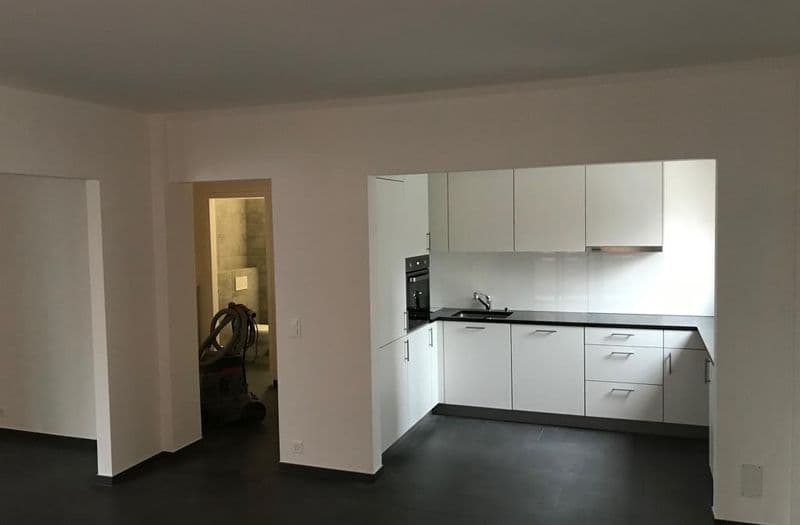 Soggiorno con cucina open space ristrutturata, mobili bianchi e pavimento in gres scuro