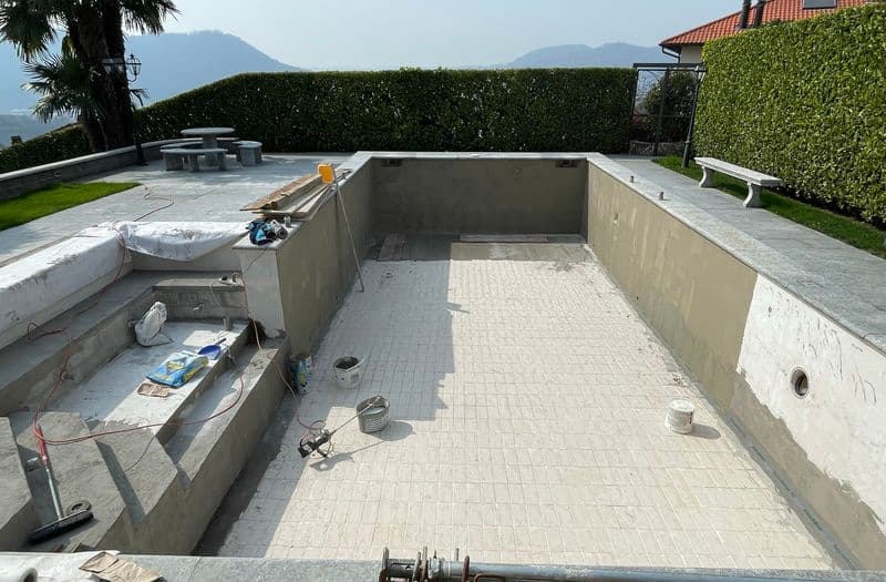 Piscina ristrutturata con rivestimento chiaro quasi ultimato, vista sulle colline di Lugano